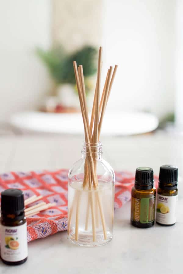 A close up of a DIY reed diffuser on a table next to essential oils.