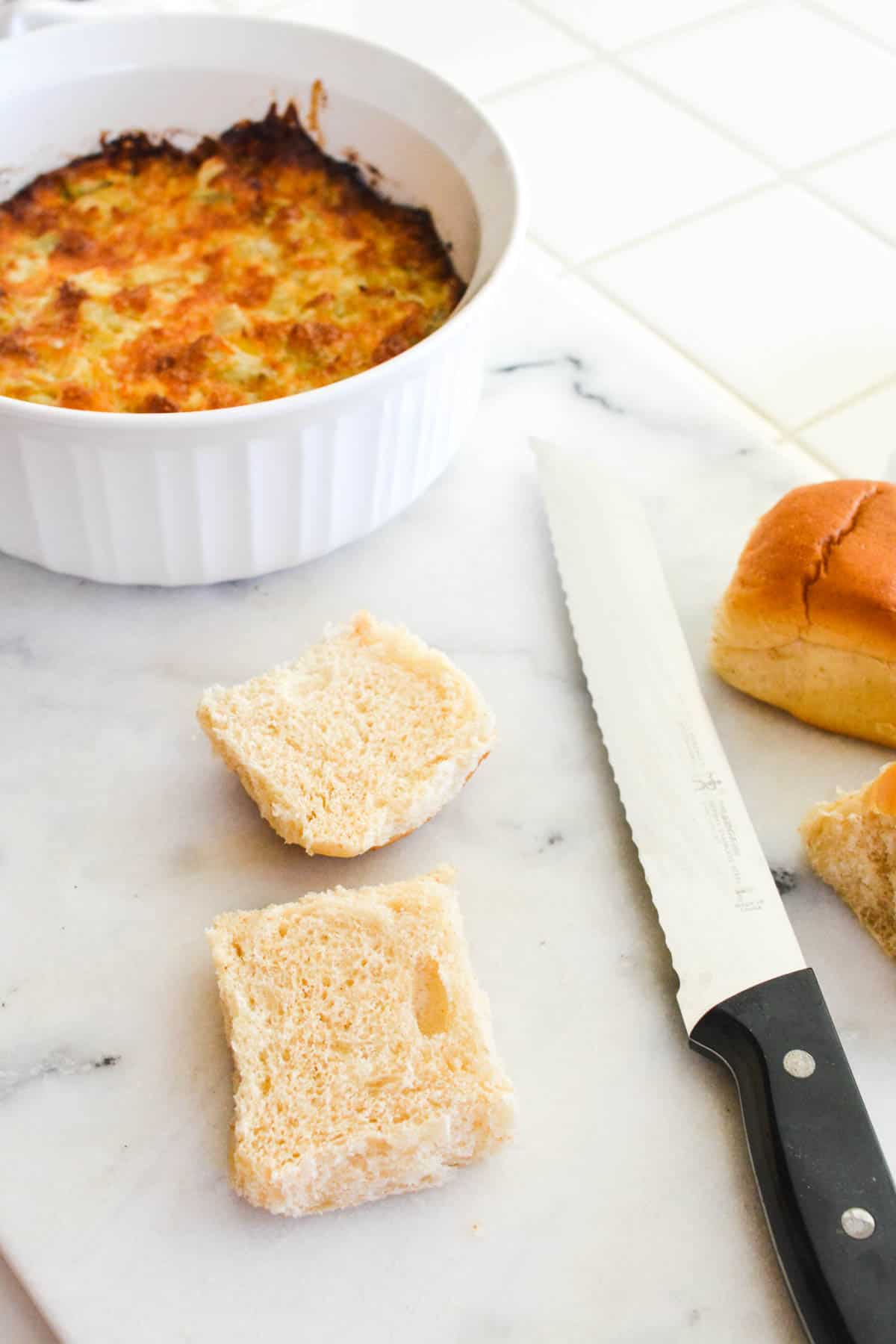 Hawaiian Roll cut in half on a cutting board next to a dish of hot artichoke dip.