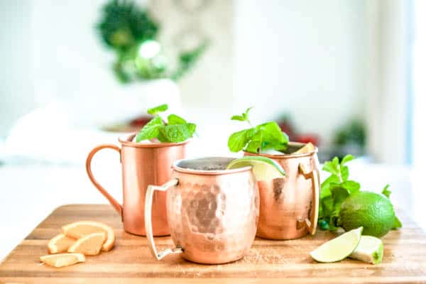 Moscow mule variations in copper mugs on a cutting board.