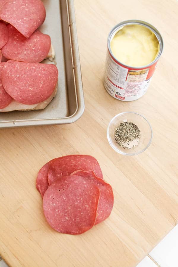 An open can of cream of chicken soup on a counter next to a baking dish with chicken topped with dried beef.