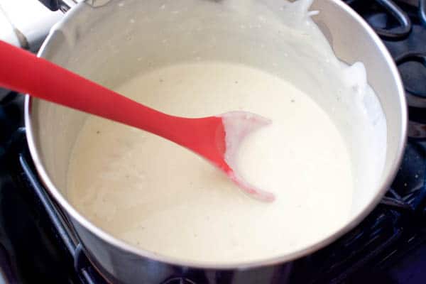A cream sauce to top chicken in a pan on the stove with red spoon. 