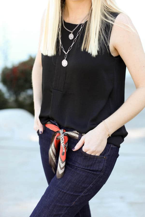 Close up of a women in black tank top with silver necklaces and a scarf worn as a belt. 