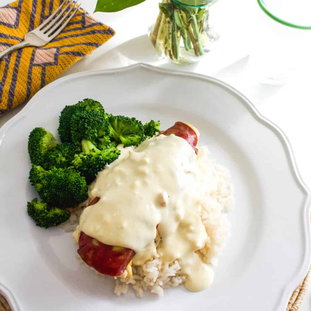 Baked chicken on a plate topped with dried beef and a cream sauce next to broccoli.