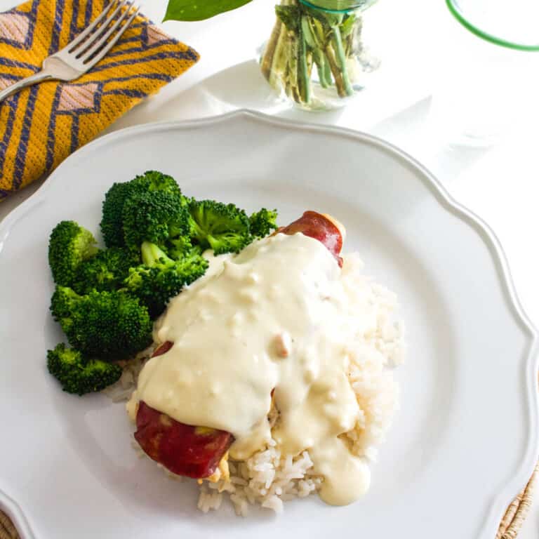 Baked chicken on a plate topped with dried beef and a cream sauce next to broccoli.