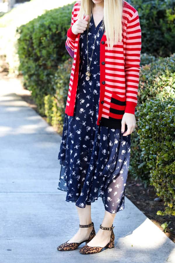 Blonde women in blue floral dress with a red and pink cardigan over it. 