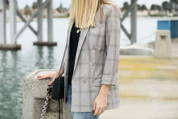 Close up of a grey plaid blazer on a woman by a lake. 