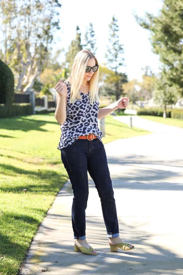 Woman in a leopard tank top can dark jeans.