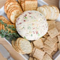 A cheese ball on a plate with crackers around it.