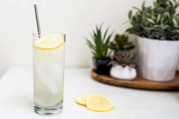 Tall cocktail in a glass with a straw on a table next to lemon slices.