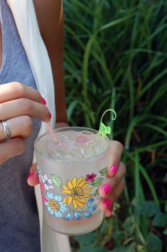Woman holding a cocktail in a floral glass with a plastic monkey garnish.