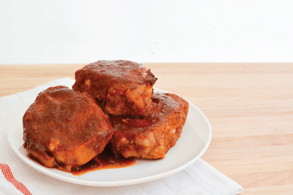 Plate of pork chops stacked and covered in a sauce.