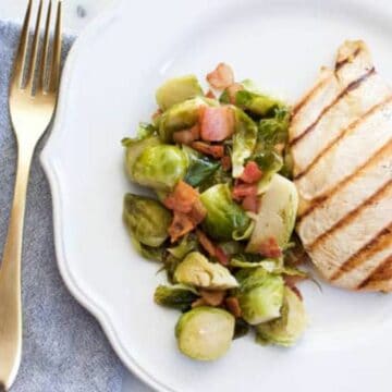 A white dinner plate with chicken and apple juice braised Brussels Sprouts.