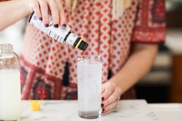 Woman adding a few drops of bitters into a cocktail glass on a counter. 