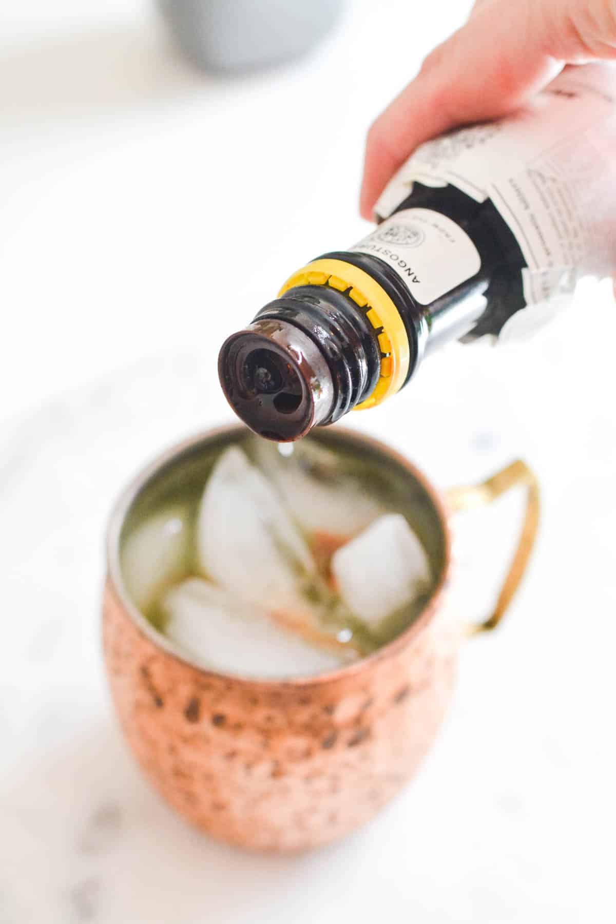 Close up of bitters being added to a cocktail in a mug.