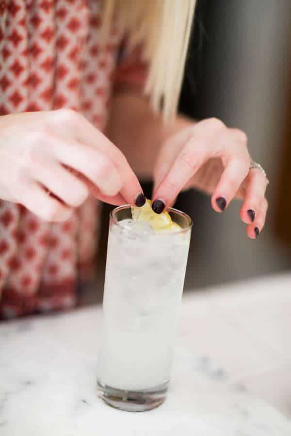 Woman adding a lemon twist garnish to a cocktail. 