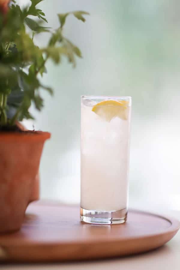 A tall cocktail glass with a lemon twist garnish sitting on a tray on a table. 
