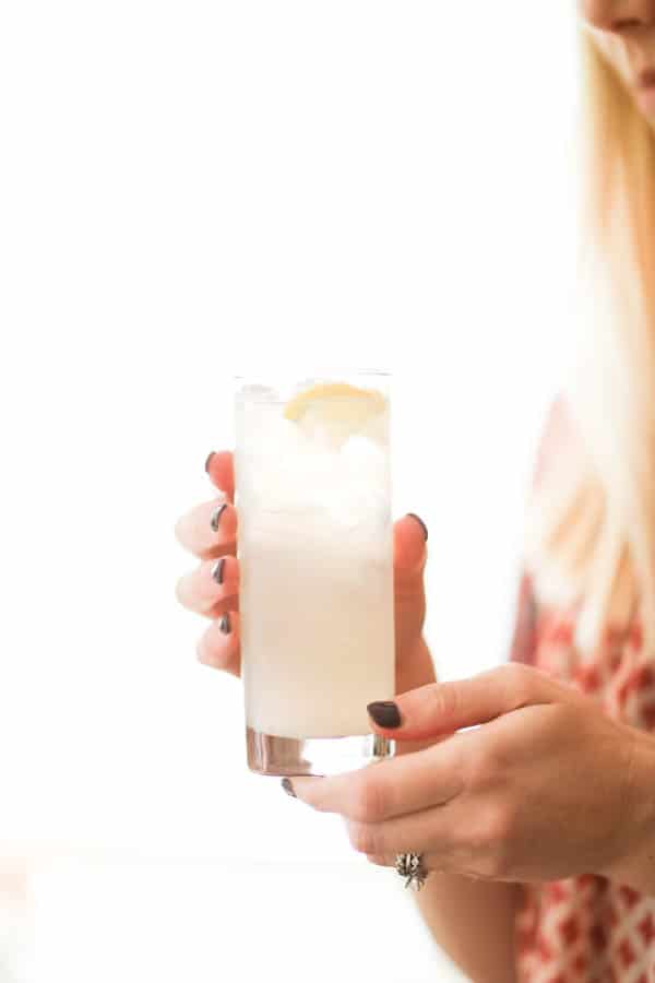 Woman holding a tall cocktail with a lemon twist. 