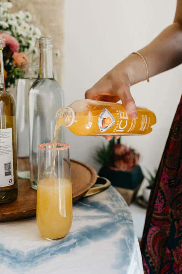 Woman adding Sparkling Ice to a fluted glass rimmed with colored sugar.