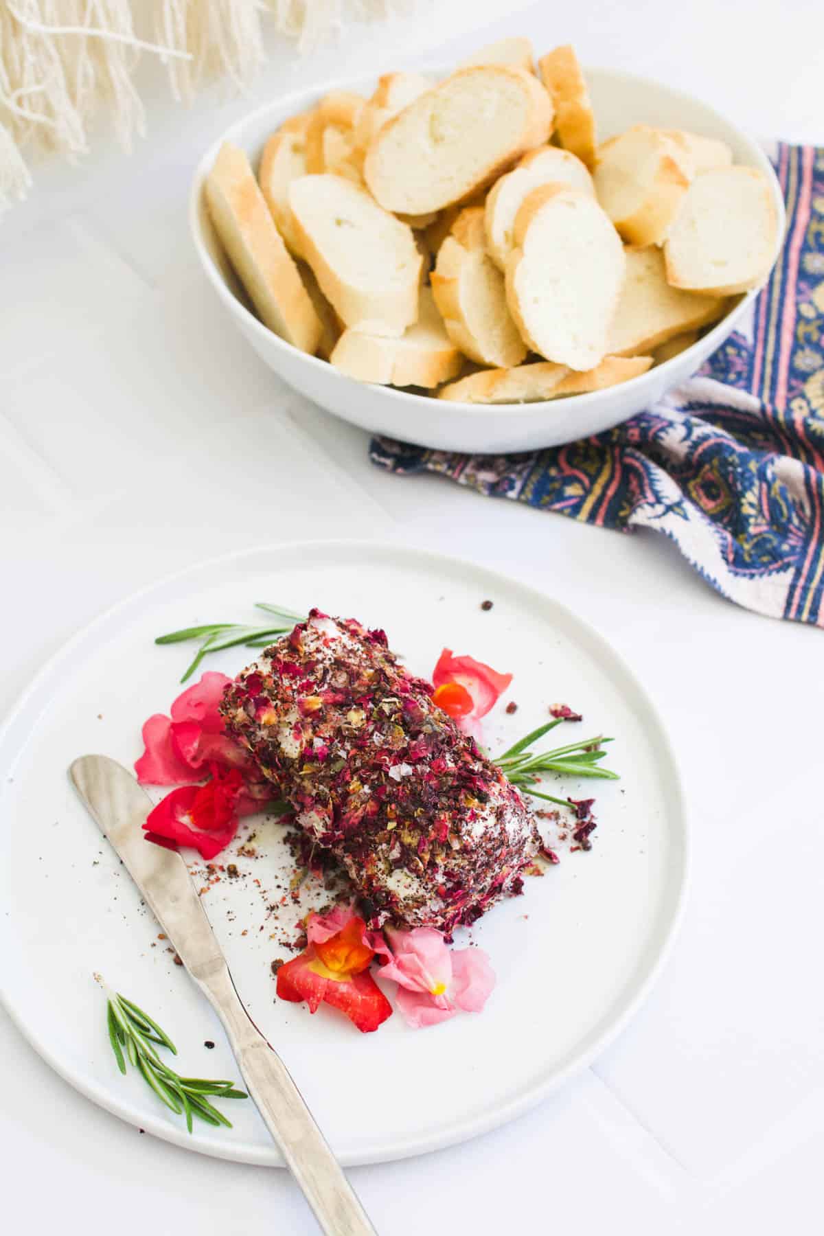 Edible flowers surrounding a savory goat cheese log on a plate next to a bowl of crostini.