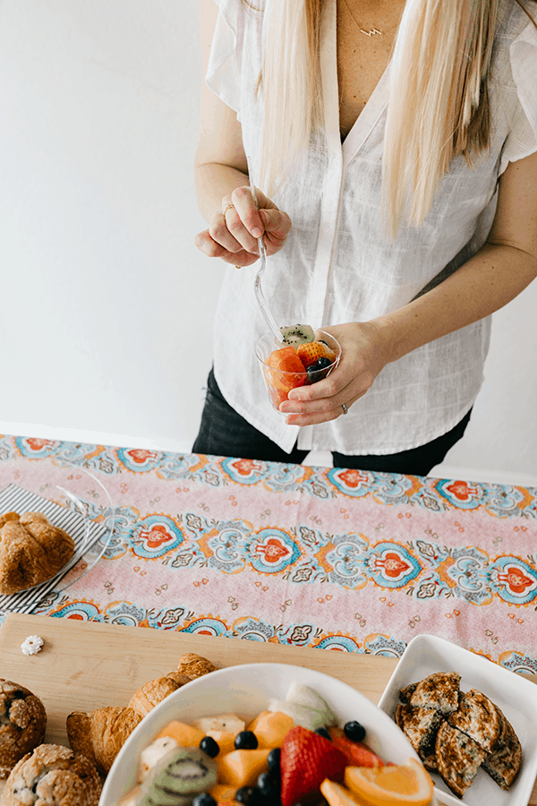 Girl holding a Chinet cup with fruit salad in it next to a brunch food table. 