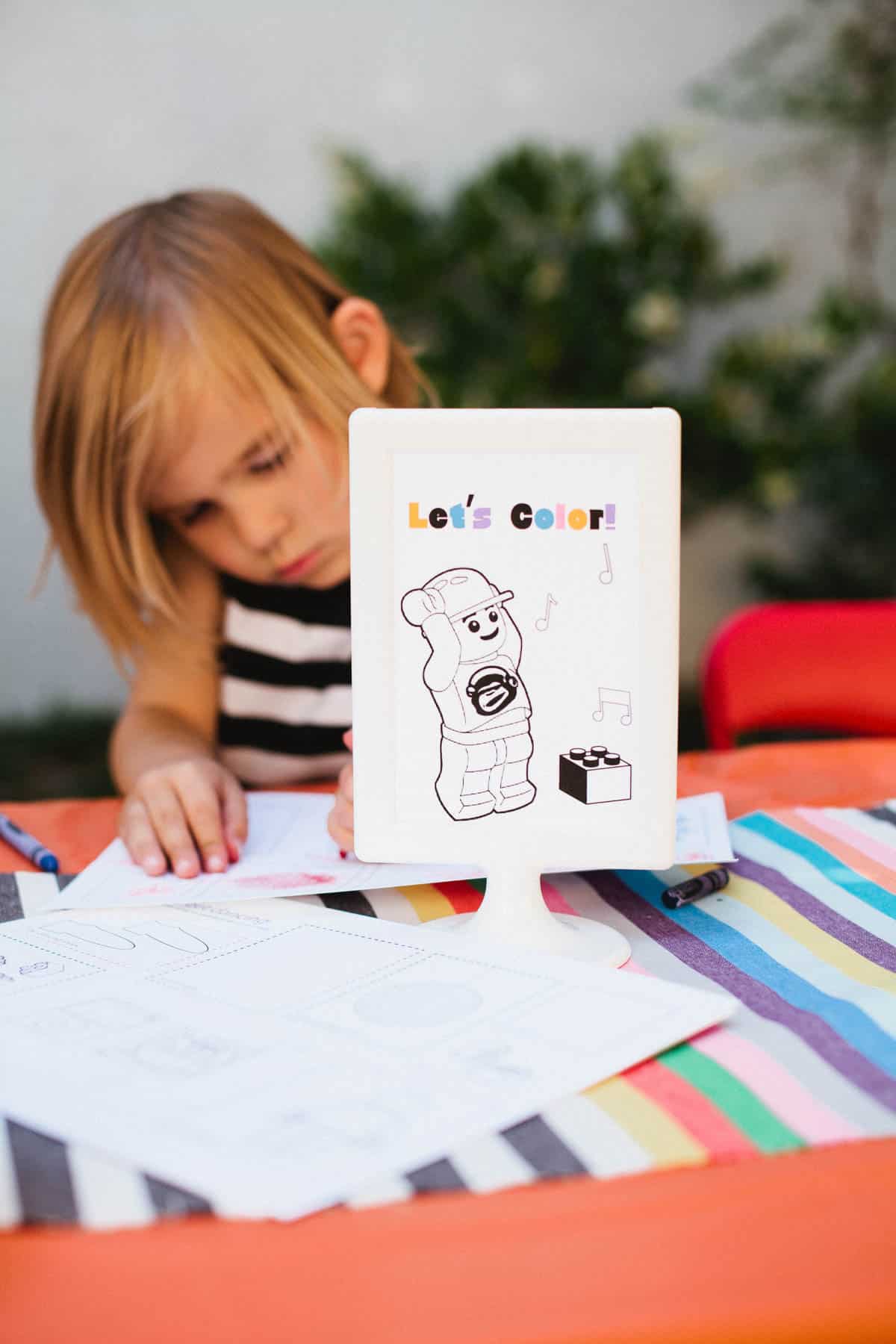 Kid coloring an activity coloring page for a lego themed birthday party.