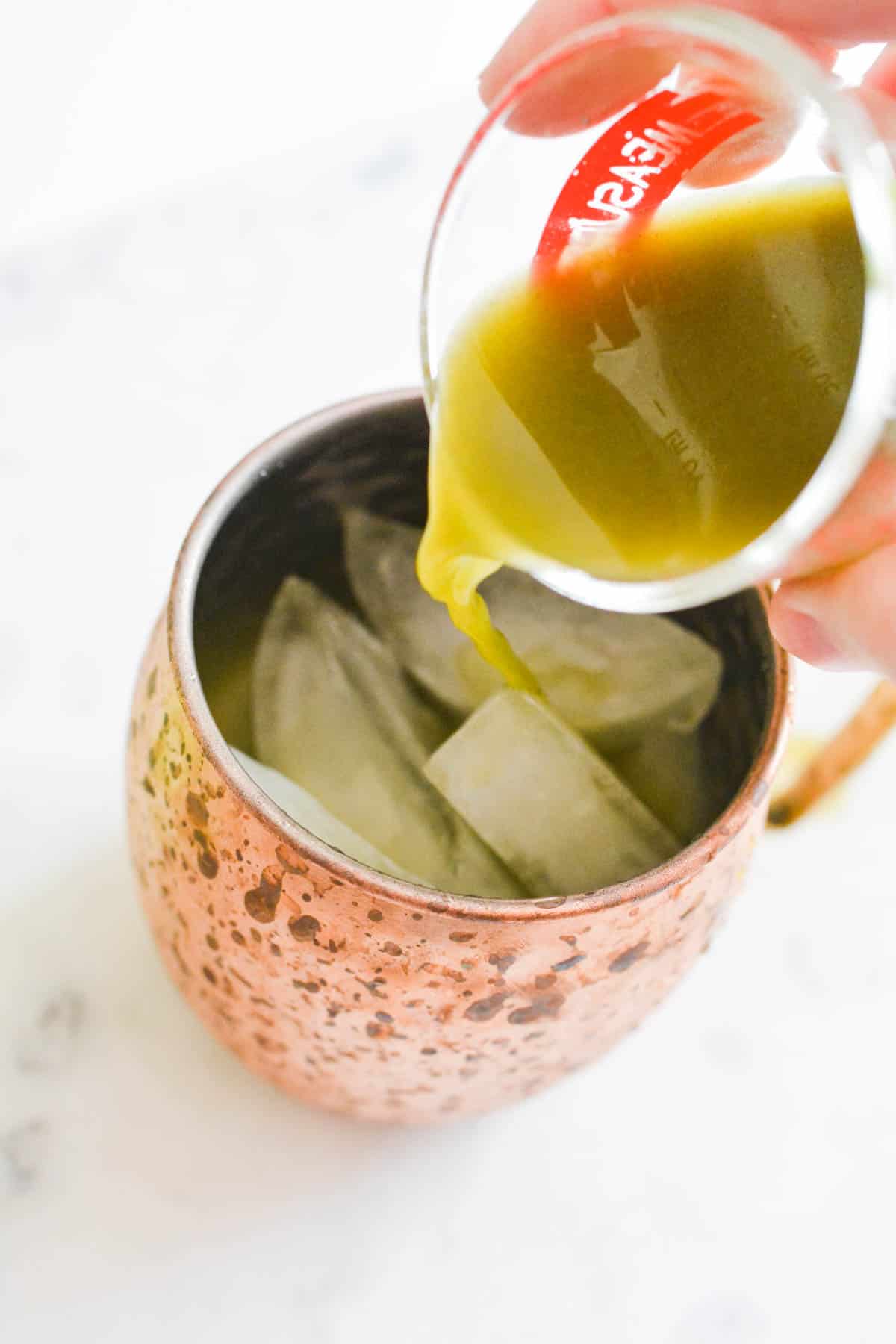 Close up of pouring green juice into a copper Moscow Mule Mug.