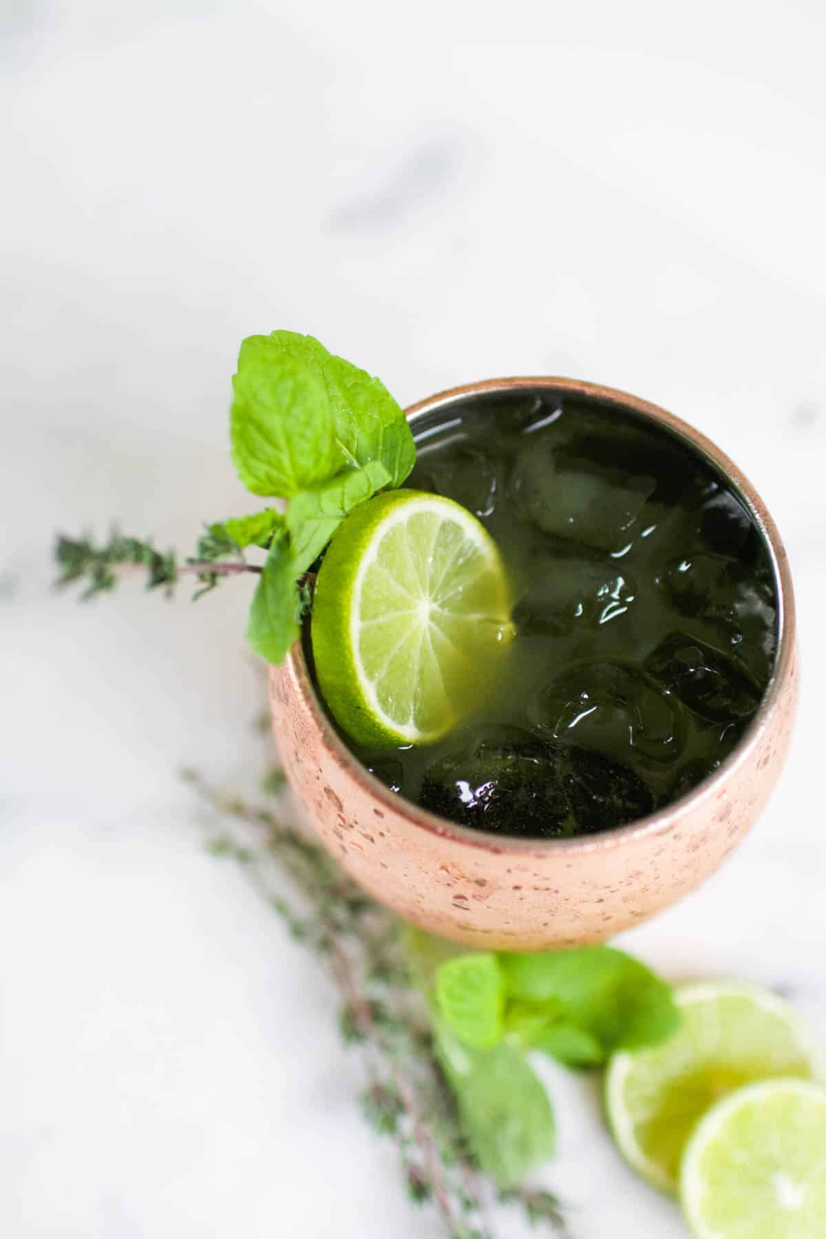 Top down view of a copper Moscow Mule mug holding a cocktail and garnished with a lime slice and fresh herbs.