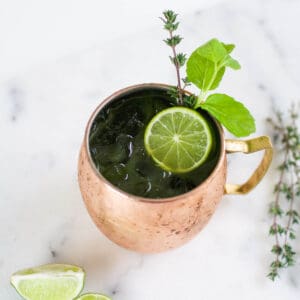 Close up of a cocktail in a copper mug with a lime and fresh herb garnish.