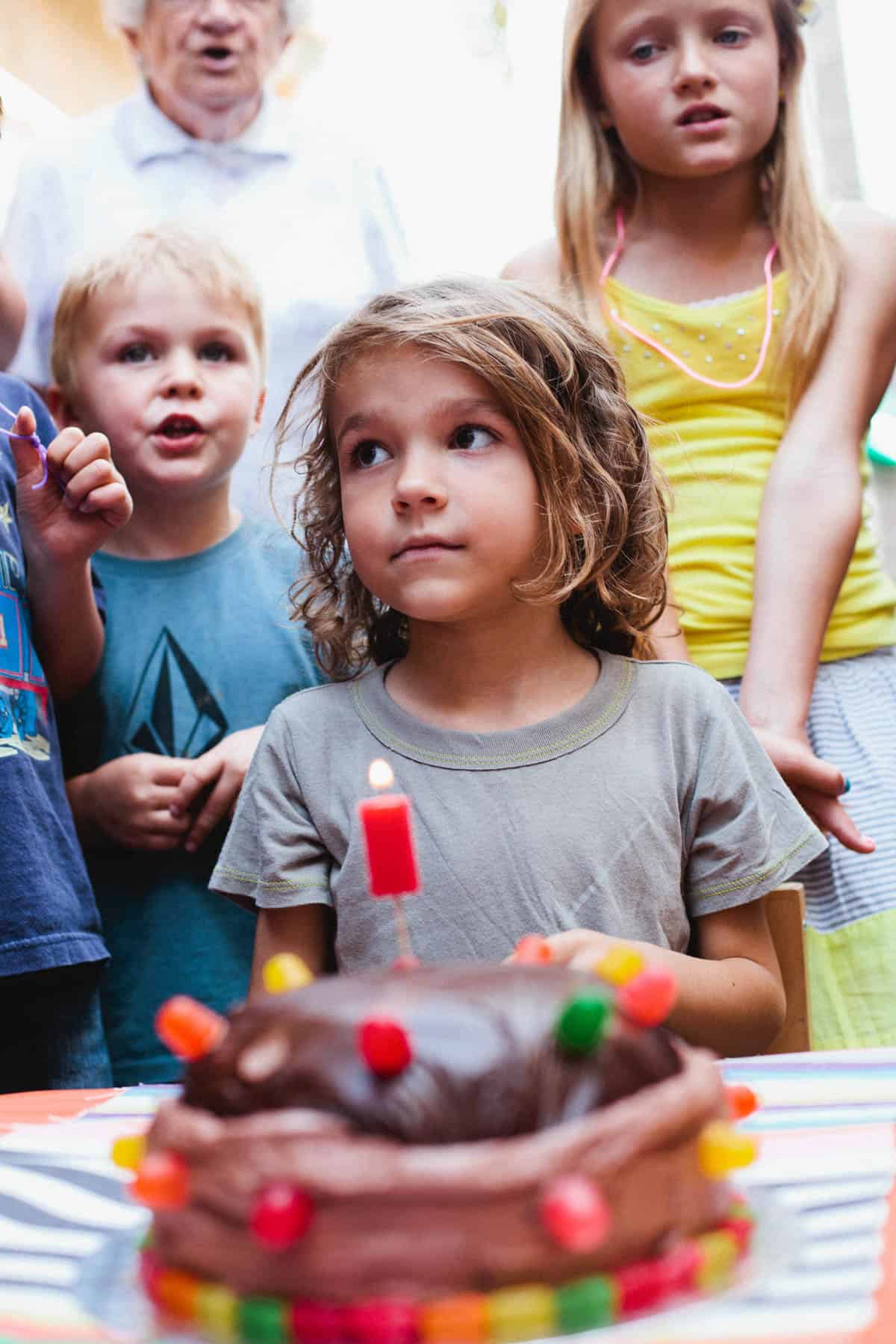 Kids singing happy birthday to a boy at a birthday party in front of his cake.