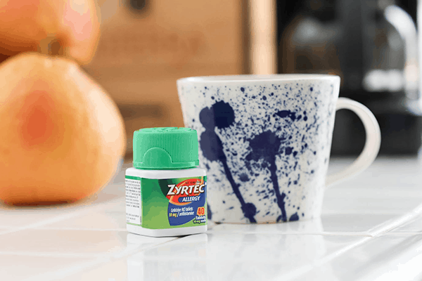 A bottle of Zyrtec on a counter next to a coffee mug.