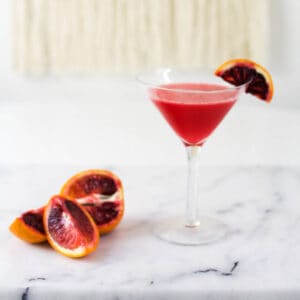 Close up of a vodka and blood orange cocktail in a martini glass.