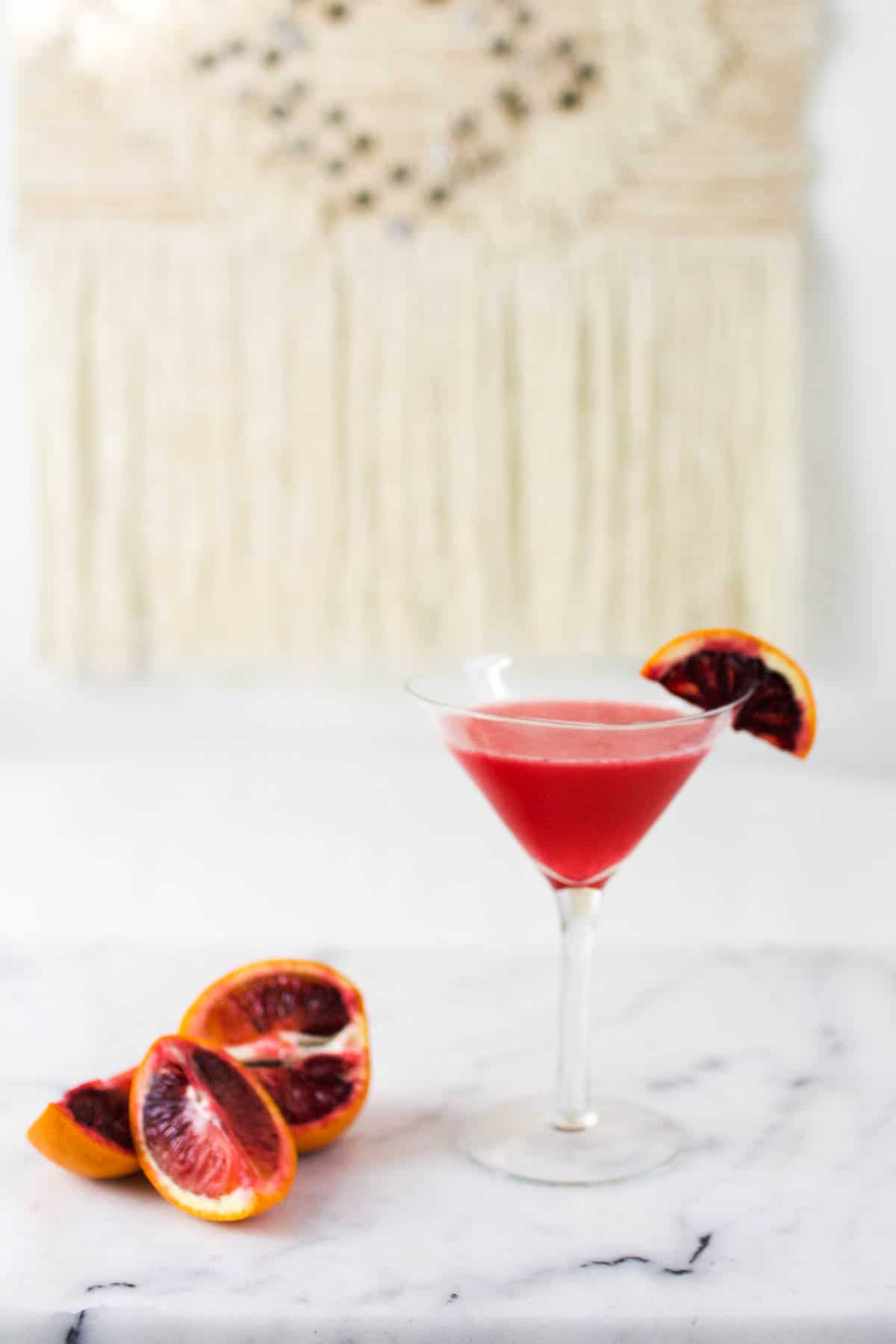 A blood orange vodka cocktail in a martini glass on a table.