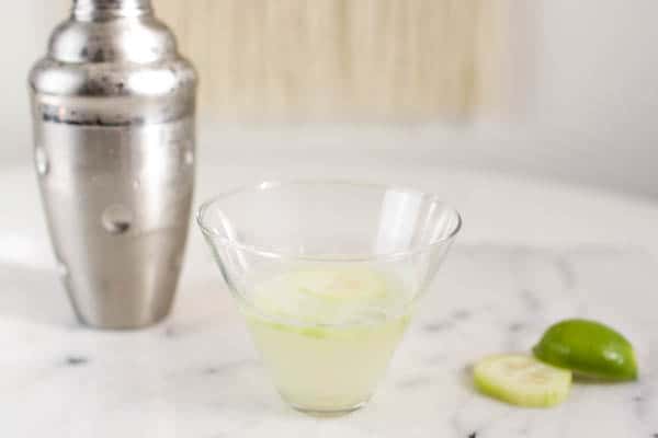 Stemless martini glass with a Cucumber Gimlet on a table next to a cocktail shaker. 