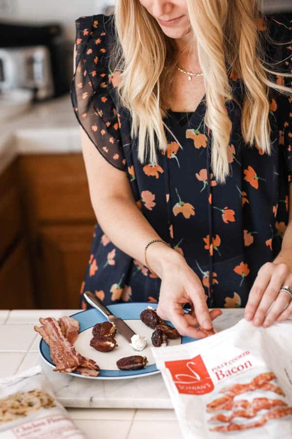 A woman sitting at counter making Bacon wrapped dates. 