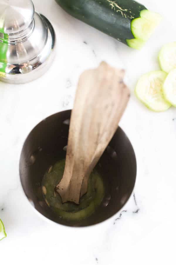 Cocktail shaker with cucumber being muddled. 