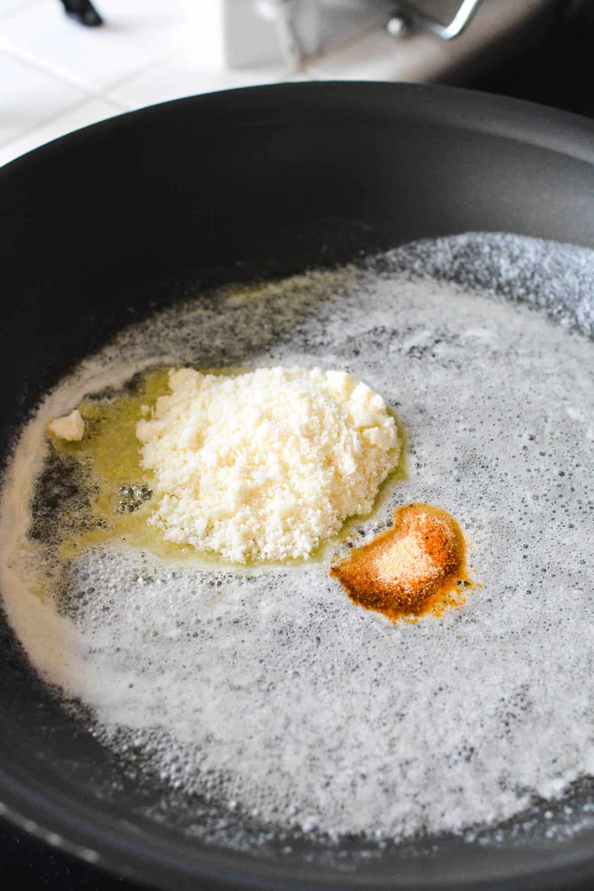 Melted butter in a pan with seasonings and parmesan cheese.