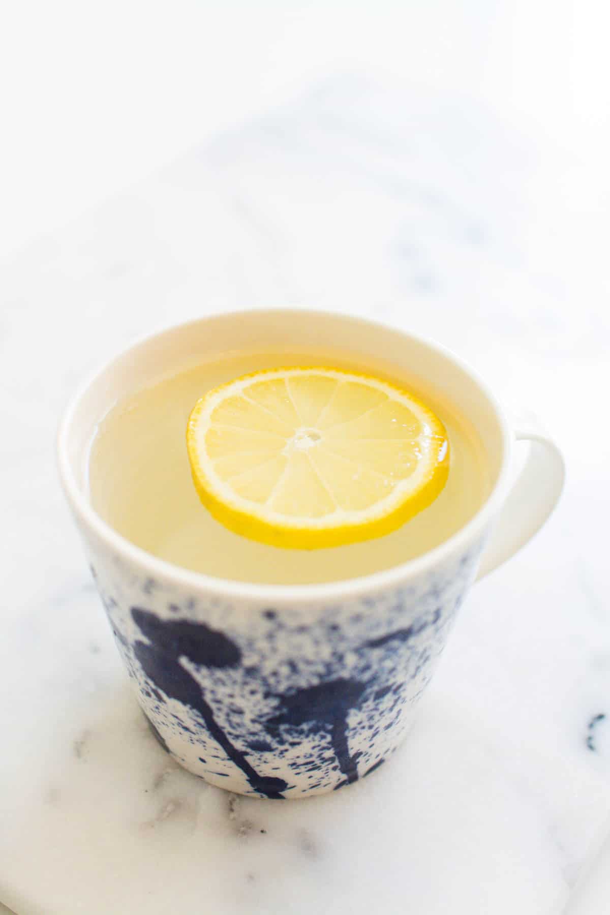 Close up of a coffee mug with water and slice of lemon floating in it.