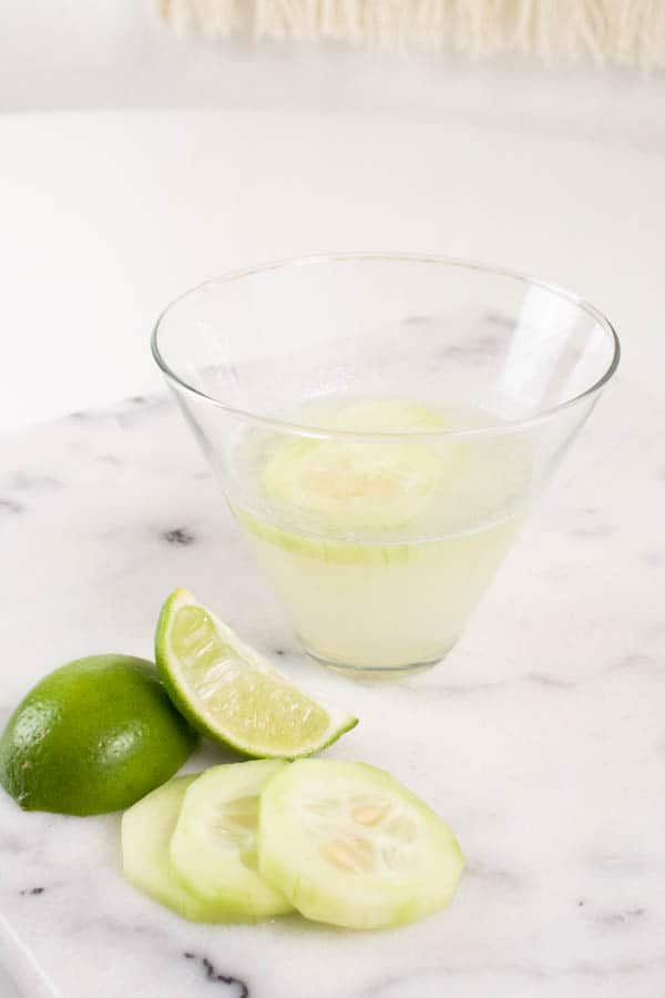 A cocktail glass with a Cucumber Vodka Gimlet cocktail in it on a table. 