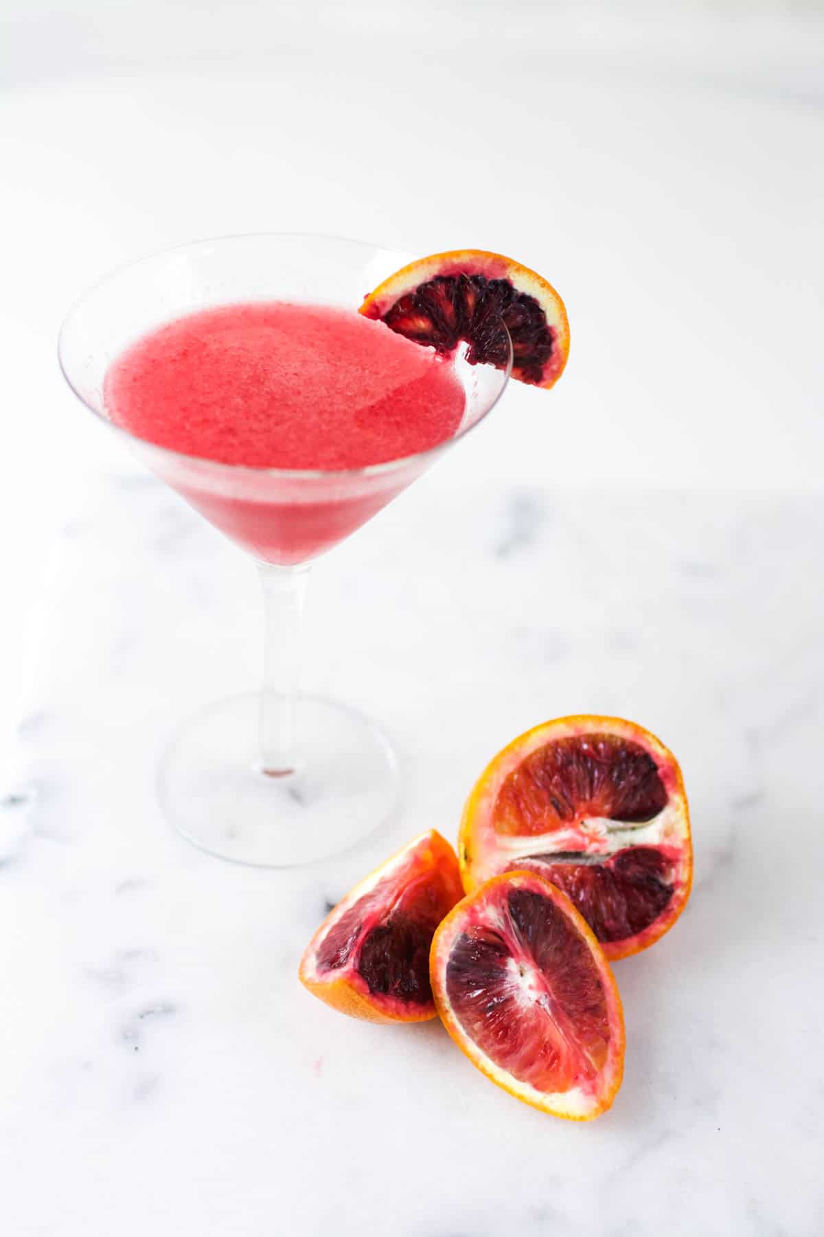 Close up of an orange martini on a table next to cut blood oranges.