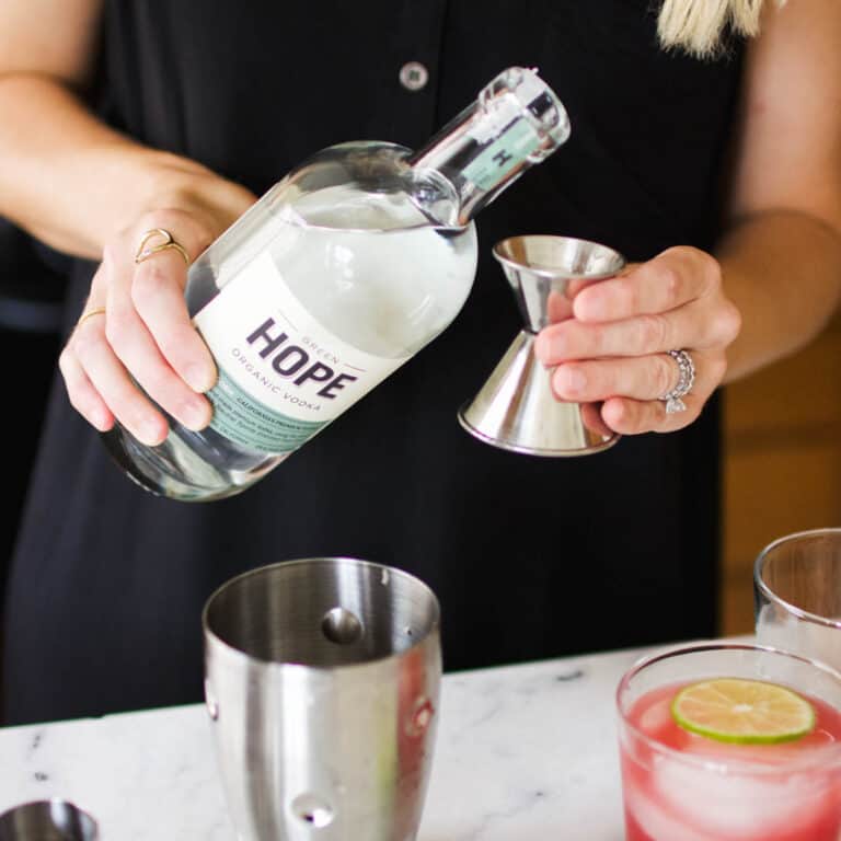 Woman pouring vodka into a jigger to make a cocktail.