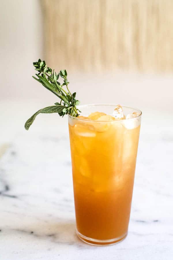 Delicious apple juice cocktail idea with vodka in a tall glass with ice and garnished with fresh herbs.