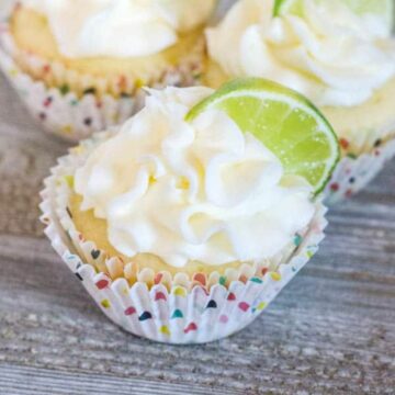 Close up of a frosted margarita cupcakes infused with tequila and topped with a lime wedge.