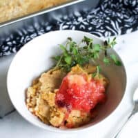 white bowl with strawberry dump cake and sprigs of thyme on a table next to a pan of dump cake