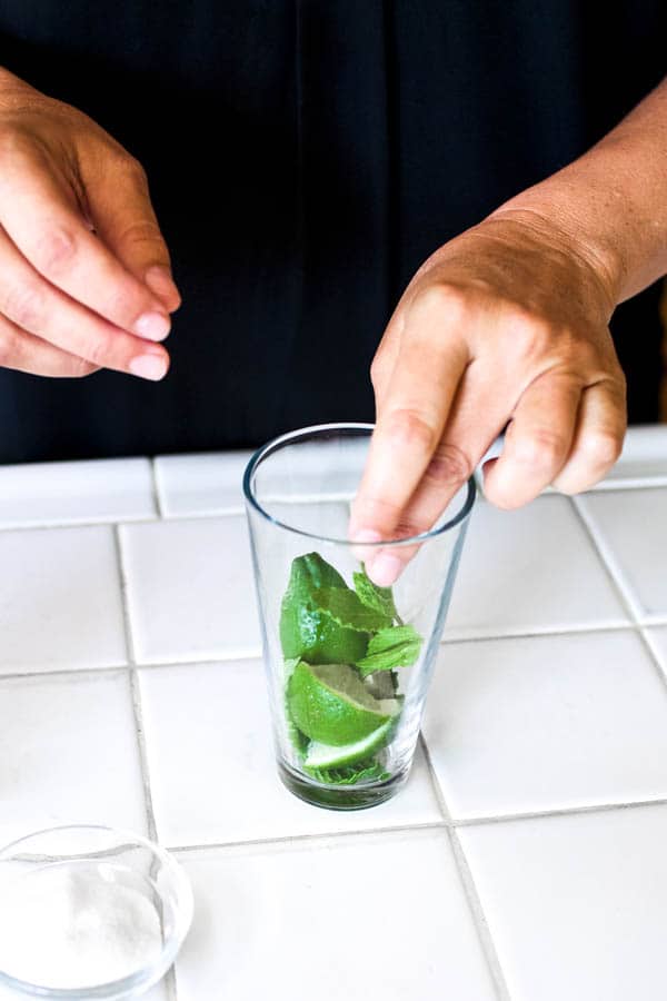Woman adding mint and limes to a glass for a mojito recipe with vodka.