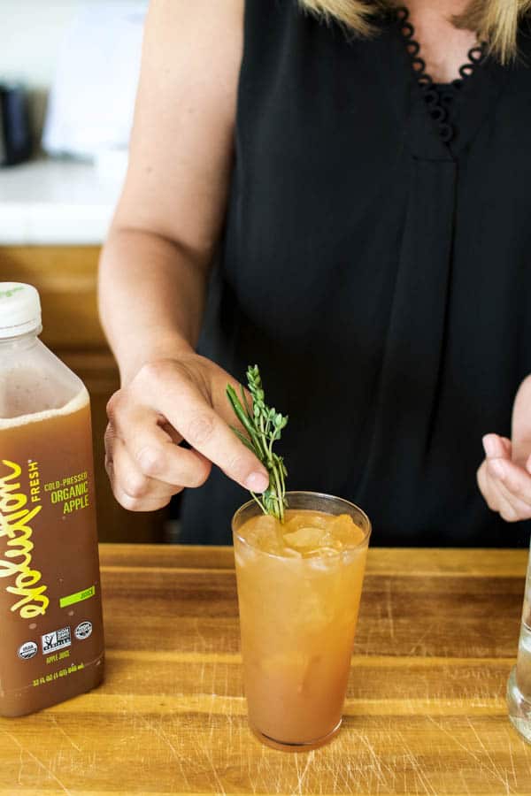 Girl adding fresh herbs to a appletini recipe idea with 2 ingredients in a tall glass.