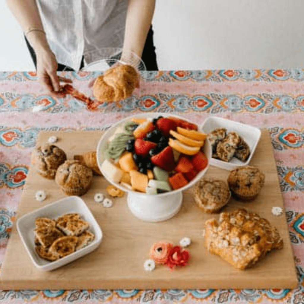 Close up of a woman holding a small plate with a croissant near food on a table for brunch.
