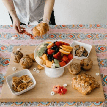 Close up of a woman holding a small plate with a croissant near food on a table for brunch.