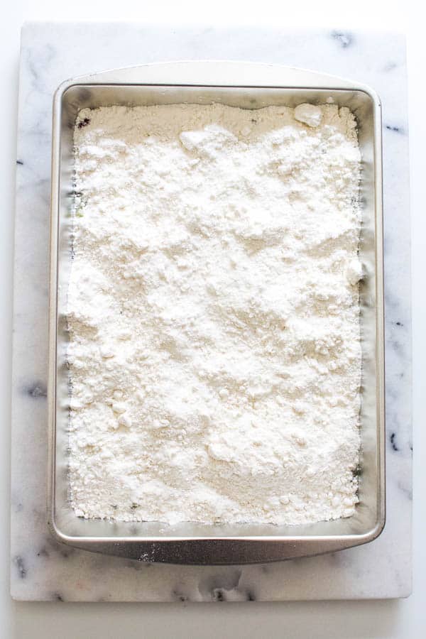 Powdered cake mix spread over fruit fillings in a cake pan on a marble cutting board.