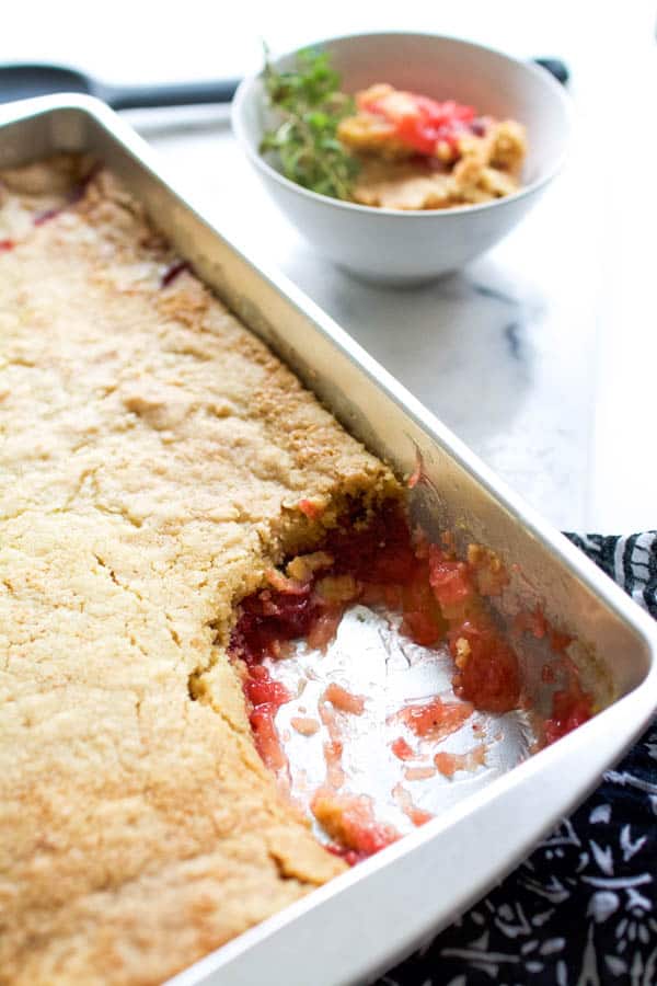 Pan of strawberry dump cake with a portion scooped out and in a white bowl in the background.