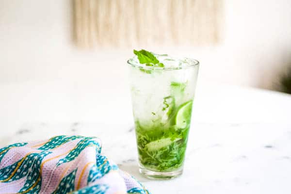 A vodka mojito in a tall glass on a table with fresh mint and lime. 